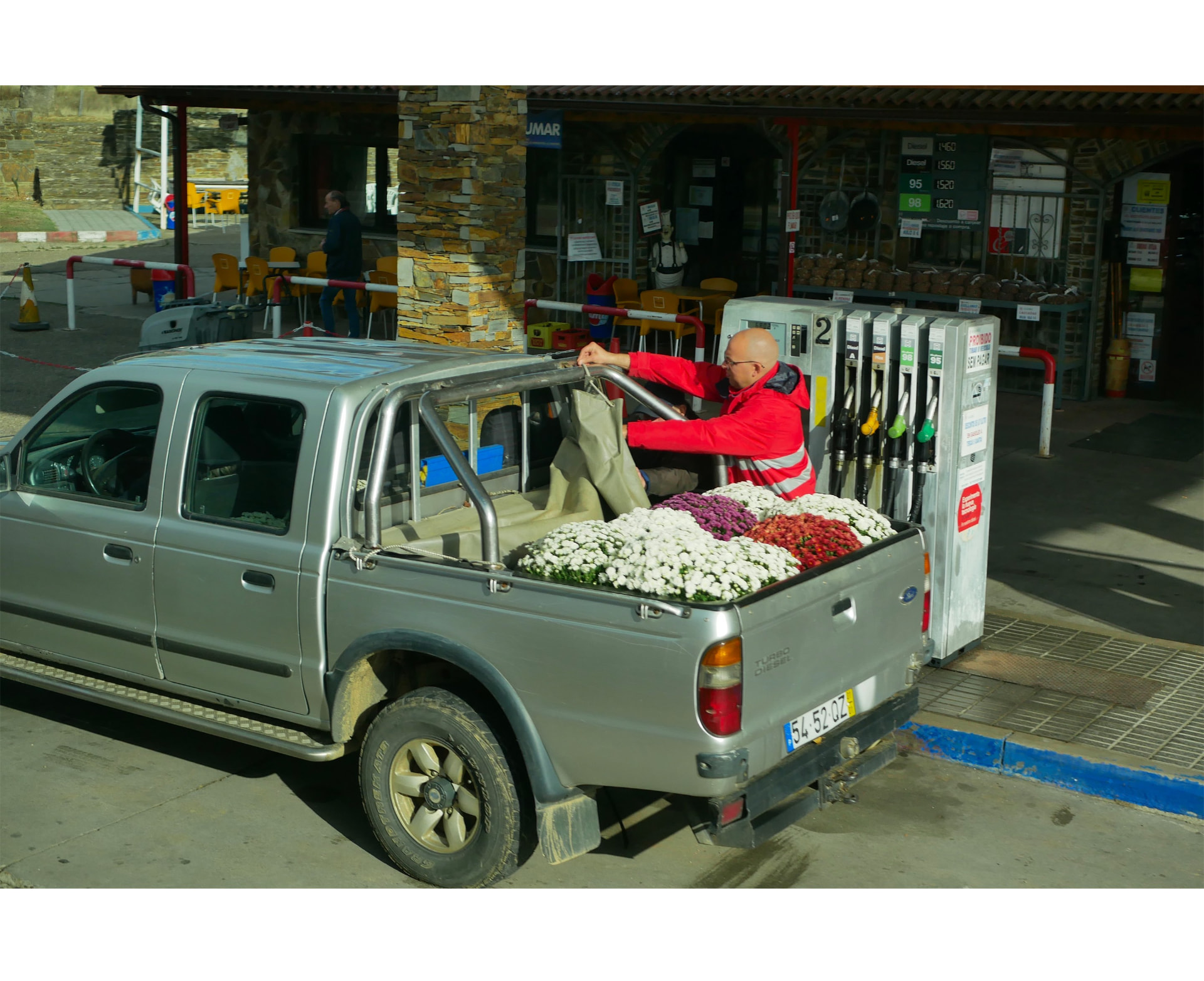 A man loading a pickup truck filled with flowers at a petrol station