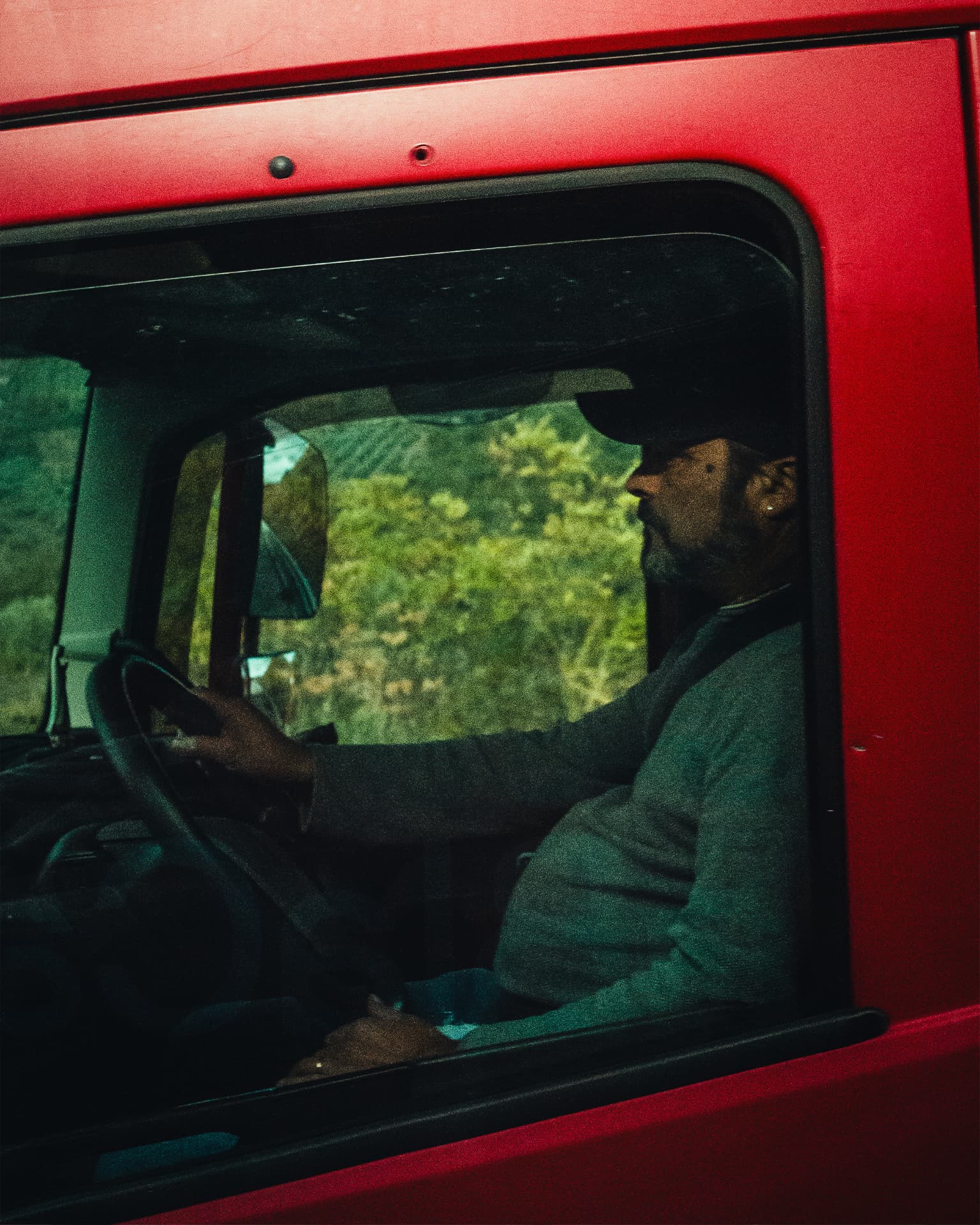A man driving a bright red vehicle, seen through the side window
