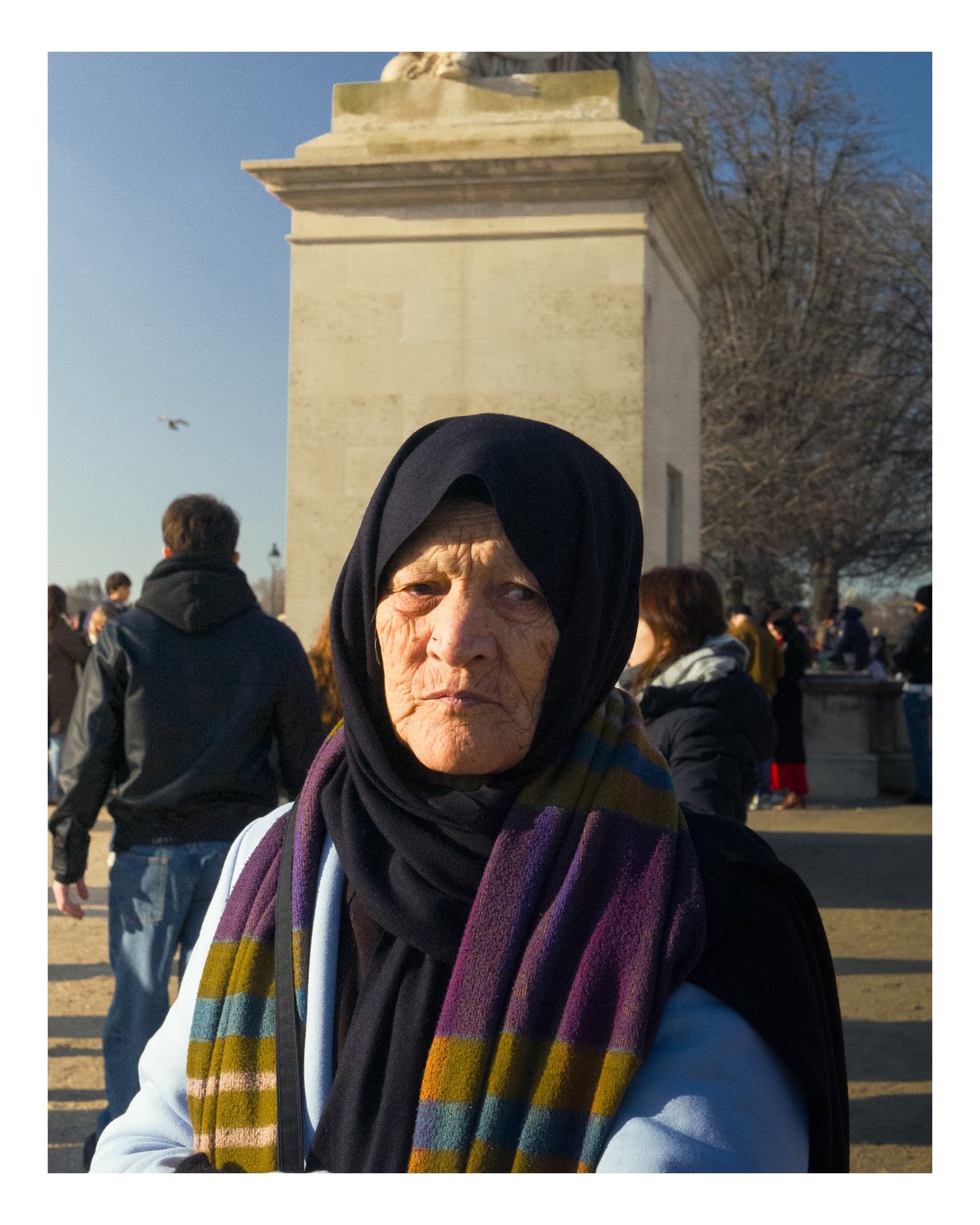Portrait of an elderly woman in a dark headscarf and colorful striped scarf