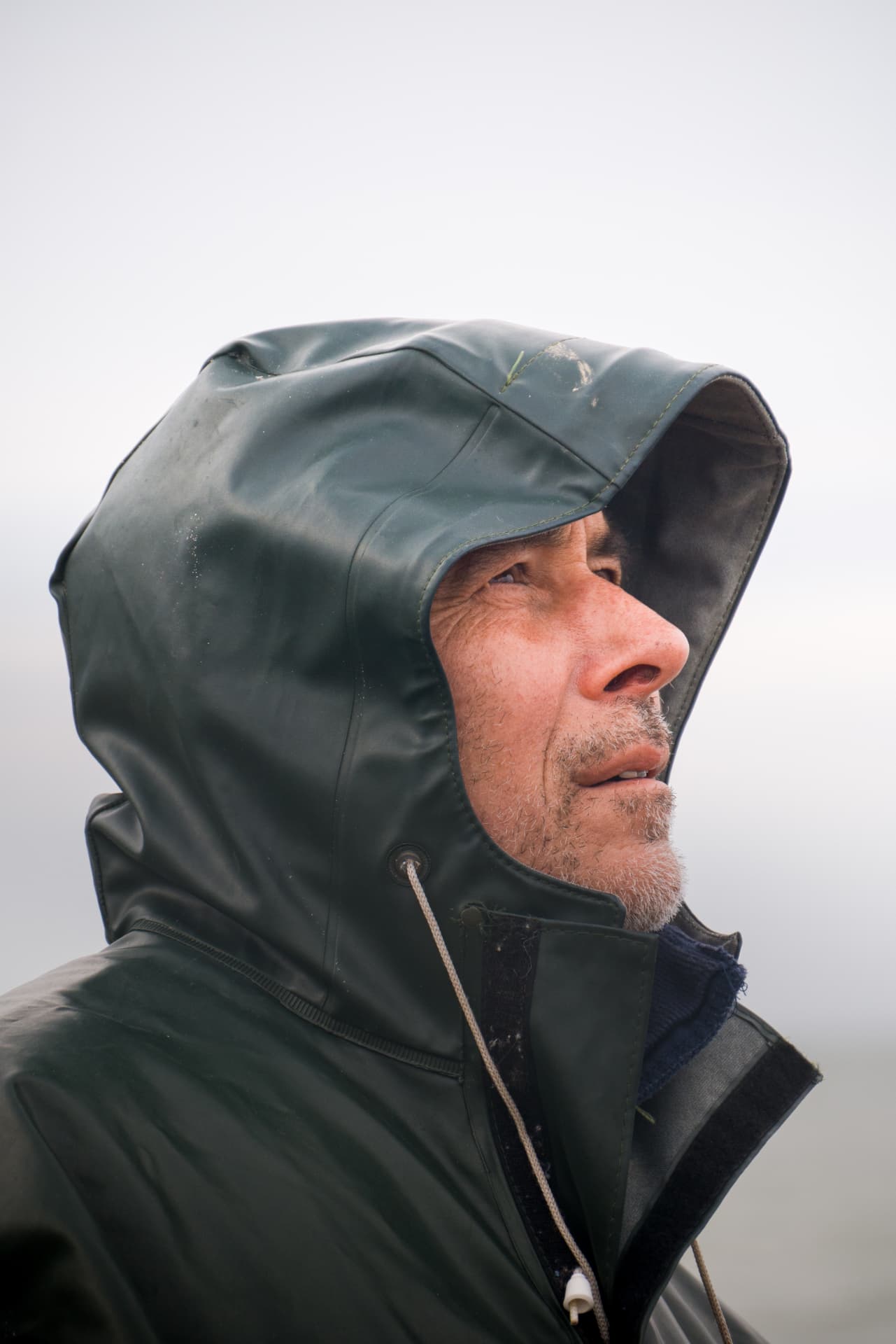 Close-up side profile of a fisherman in a dark green hooded raincoat