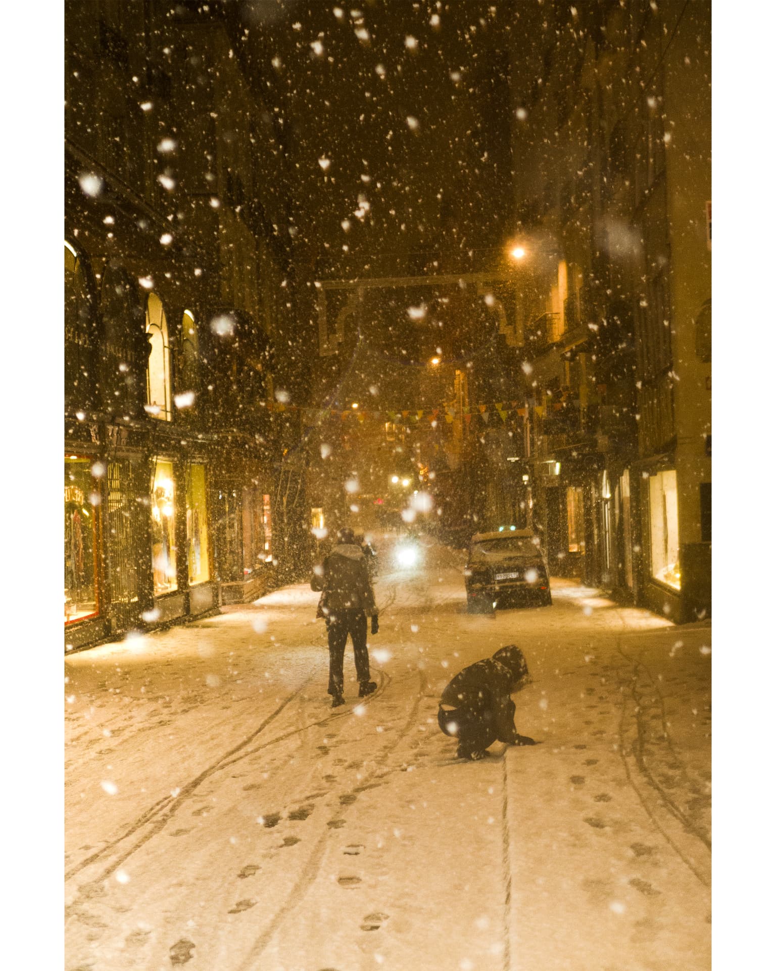 A snow-covered city street lit by warm yellow lights