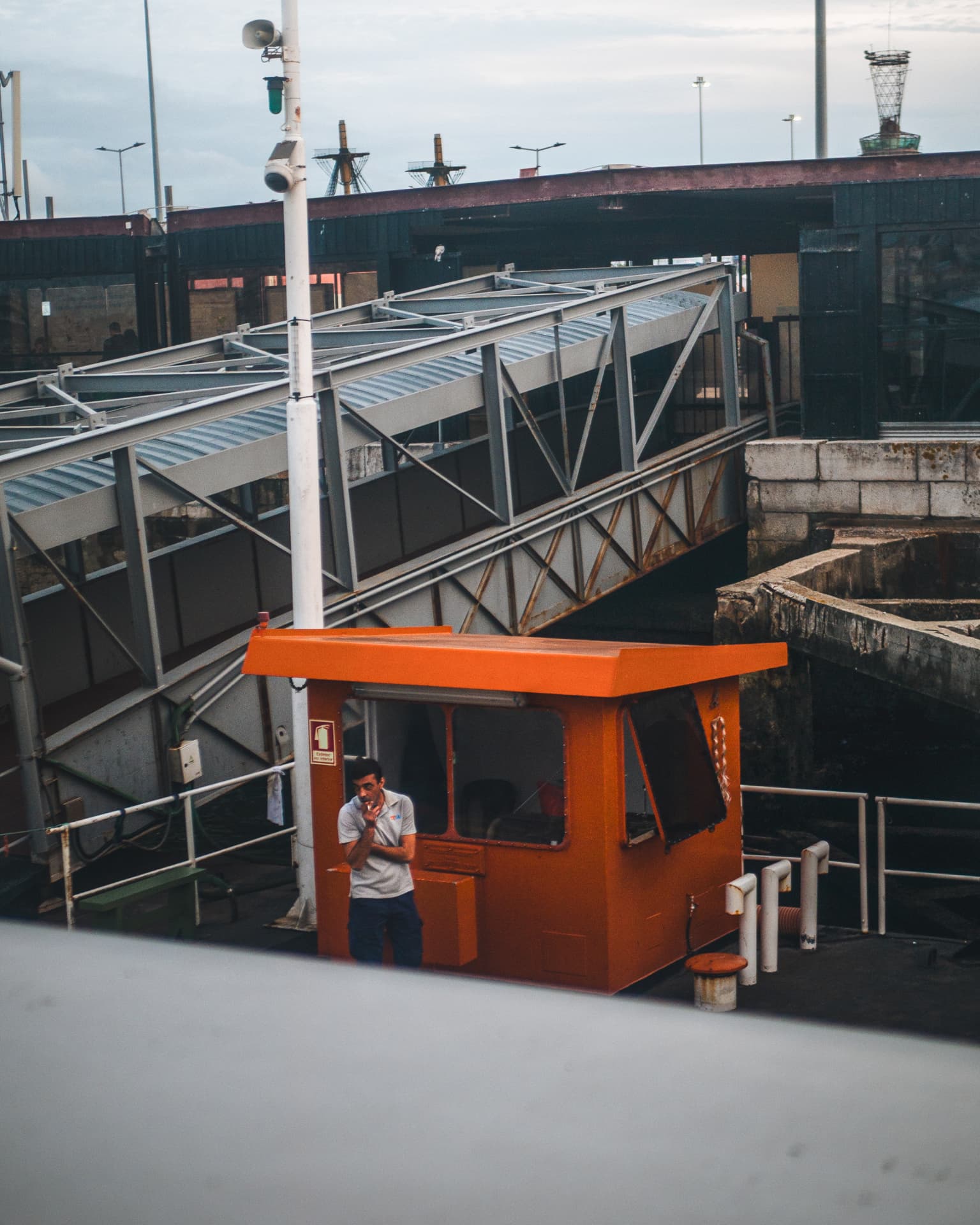A man standing beside a small orange structure at the port